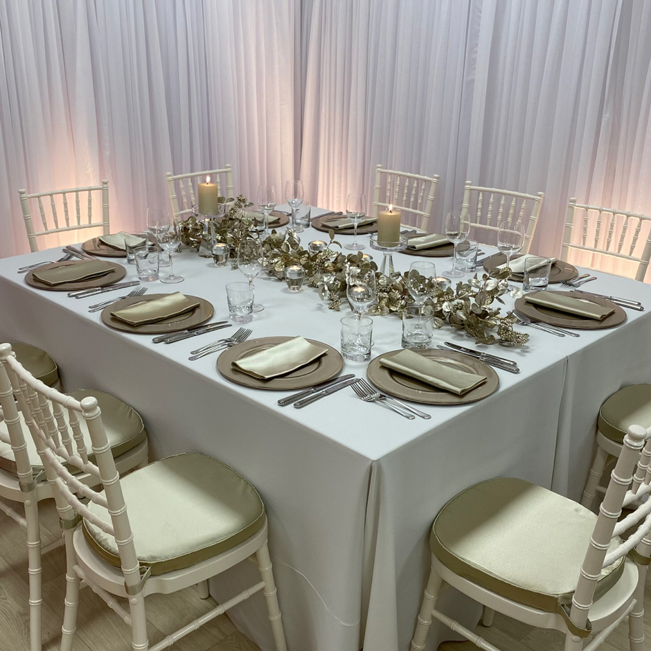 Styling features: Ivory Chiavari chairs w/sand Milano pads, white Essential linen, sand Milano napkins, latte Metallic chargers and Riedel glasses.