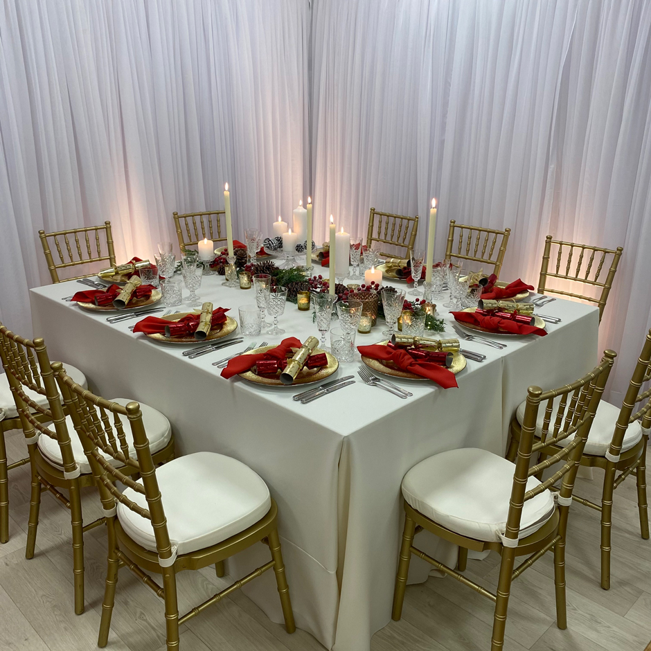 Styling features: Gold Chiavari chairs w/cream Essential pads, cream Essential linen, red Essential napkins, gold Starburst chargers and Cut Crystal glasses.