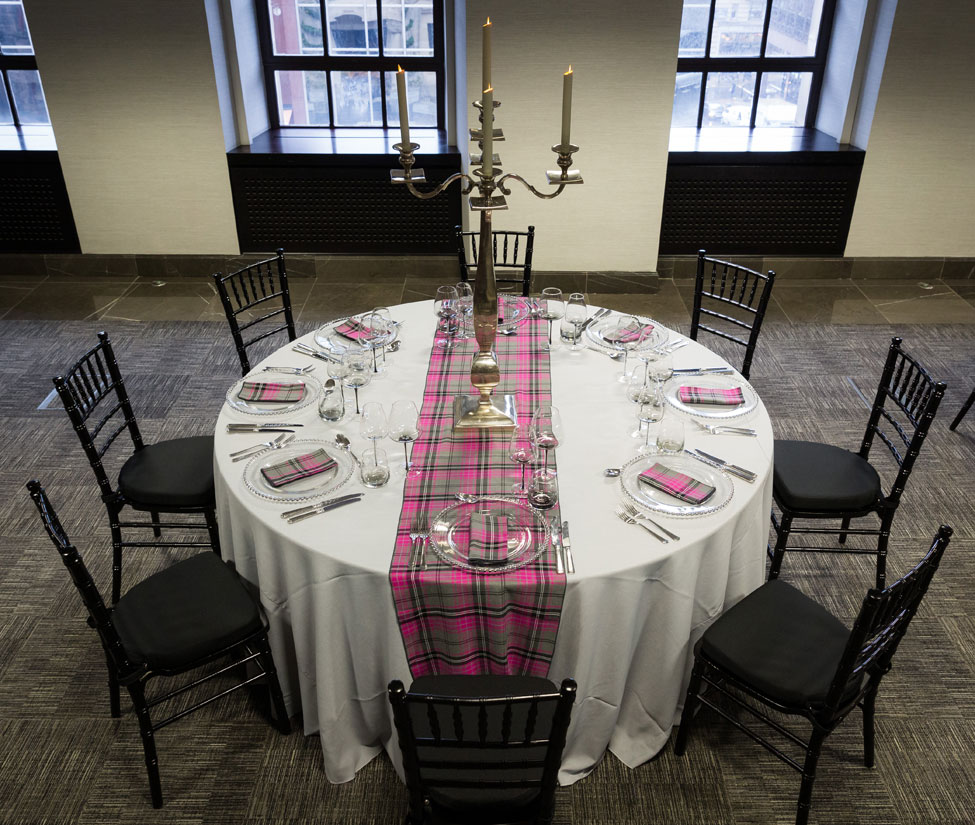Styling featuring Grigio Gelato table linen, Silver Beaded charger plates paired with Iona Tartan napkins and table runner, Smoke Grey glasses, Silver Square Base Candelabra and Black Chiavari Chairs with Black Essential seat pads