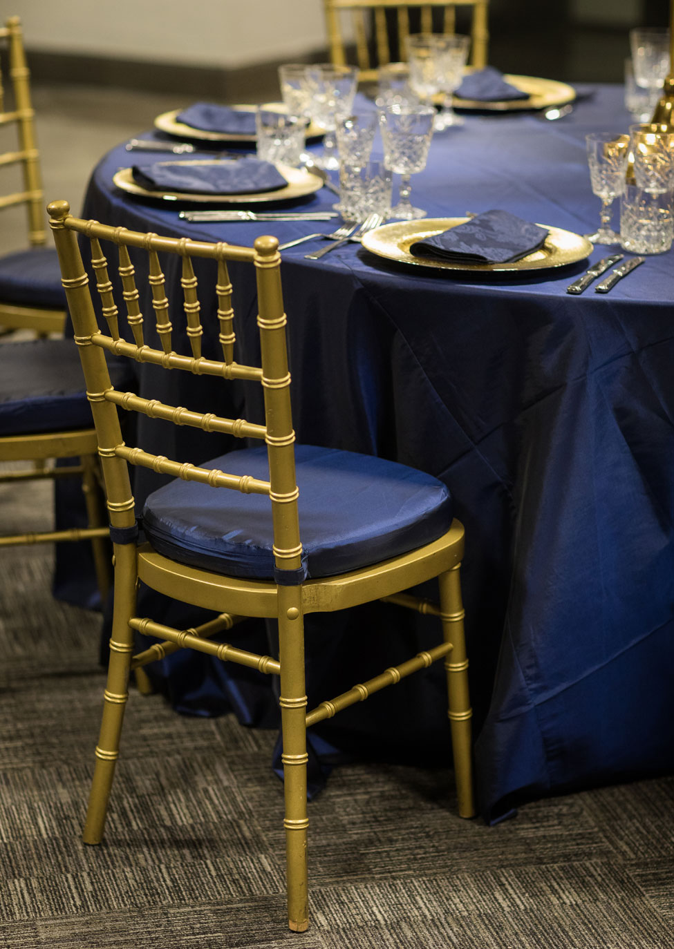 Styling featuring Midnight Blue Taffeta table linen, Gold Starburst charger plates paired with French Navy Vintage Damask napkins, Cut Crystal glasses, Gold Candelabra and Gold Chiavari Chairs with Midnight Blue Taffeta seat pads