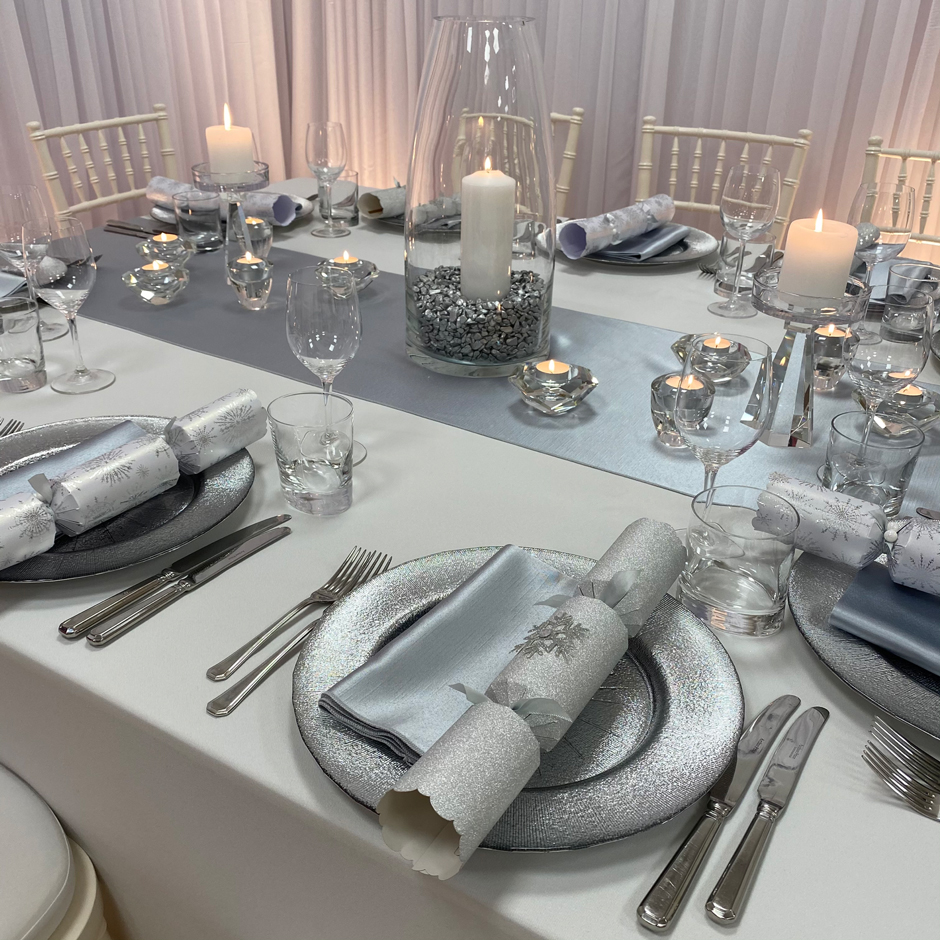 Styling features: Ivory Chiavari chairs w/white Essential pads, white Essential linen, silver Milano runner & napkins, silver Starburst chargers and Riedel glasses.