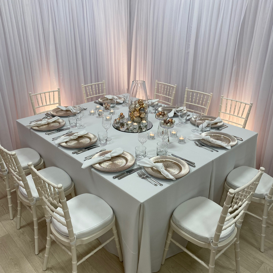 Styling features: Ivory Chiavari chairs w/white Essential pads, white Essential linen & napkins, rose gold Starburst chargers and Riedel glasses.