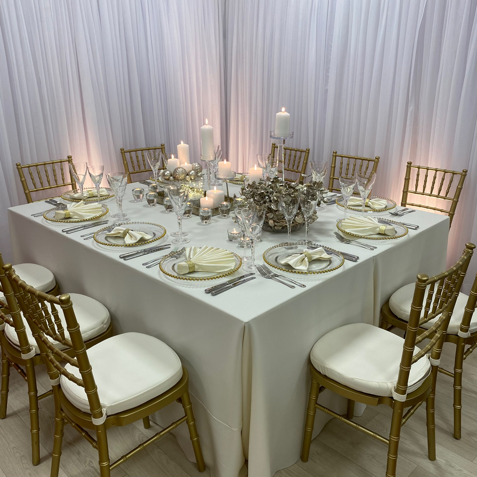 Styling features: Gold Chiavari chairs w/cream Essential pads, cream Essential linen, vanilla Milano fan & bow-tie napkins w/gold napkin rings, gold Beaded chargers and Swirl glasses.
