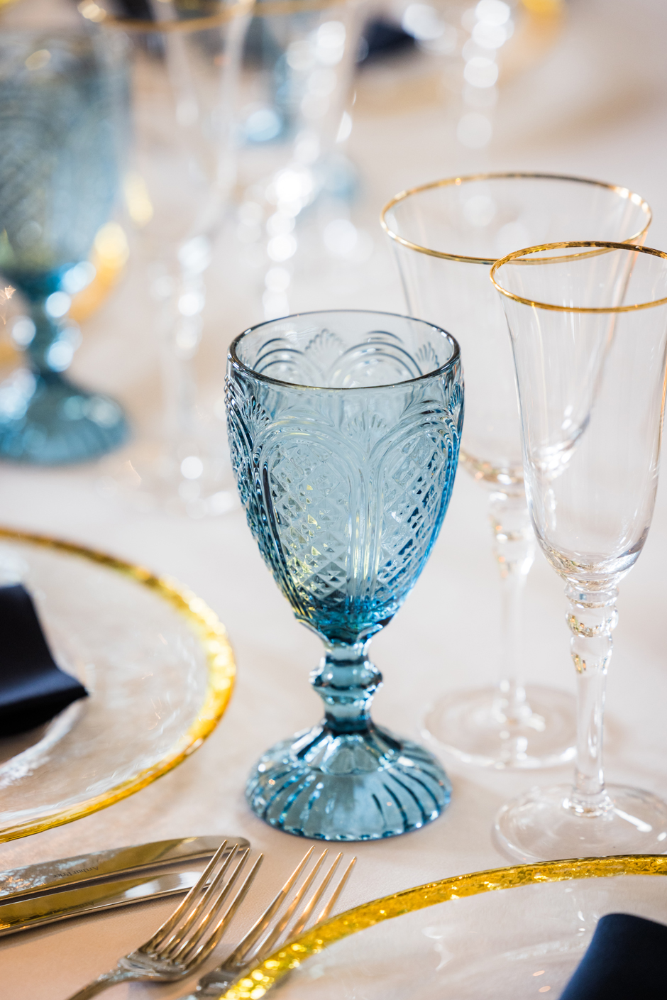 Blue goblet with white Essential linen, navy Essential napkin, gold trim charger plate & gold trim glasses